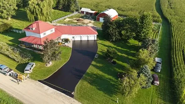 Country home driveway with fresh black sealcoating and red metal roof in Iowa